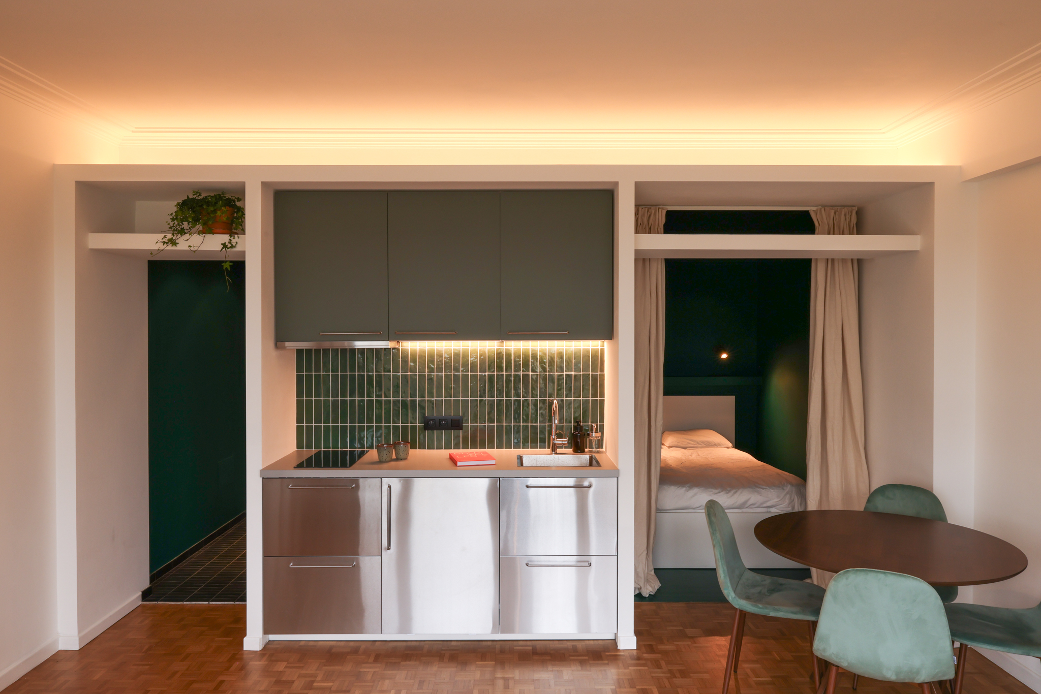 rénovation studio Bruxelles, lit dans un niche vert foncé, cuisine inox, carrelage bejmat vert