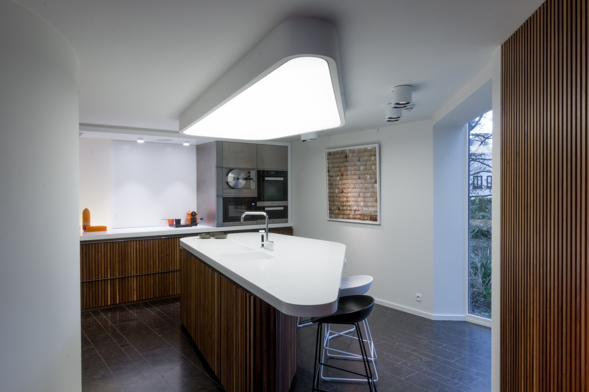 Cuisine moderne bois et plan de travail Corian avec îlot triangulaire dans une villa