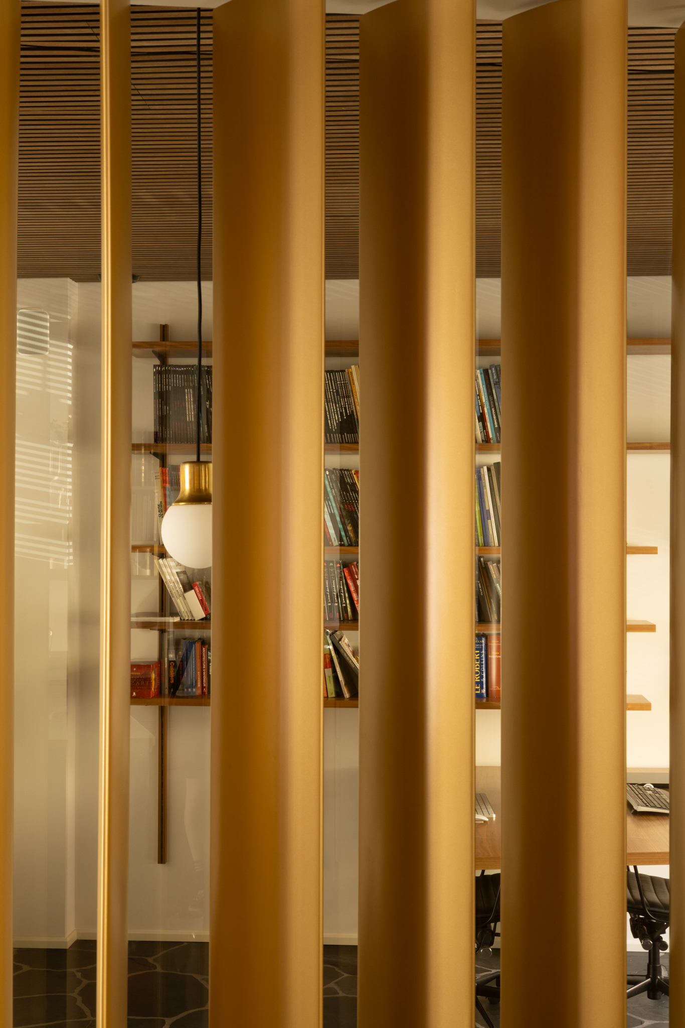 Claustra en laiton et parois vitrées dissimulant un espace bureau adjacent à la cuisine, une rénovation intérieure.