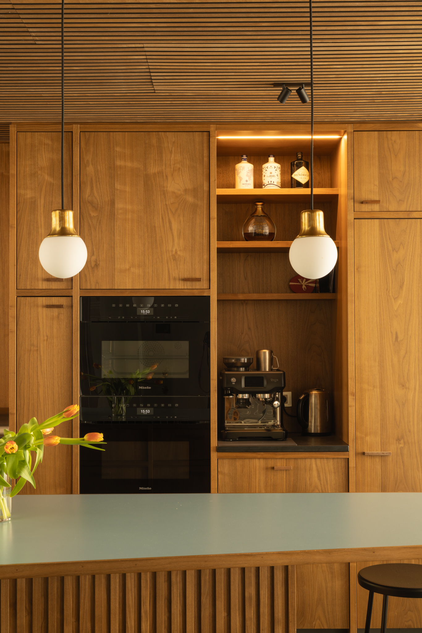 Cuisine en noyer sur mesure avec plans de travail en stratifié noir et bleu pâle, îlot central intégré autour d’une colonne existante