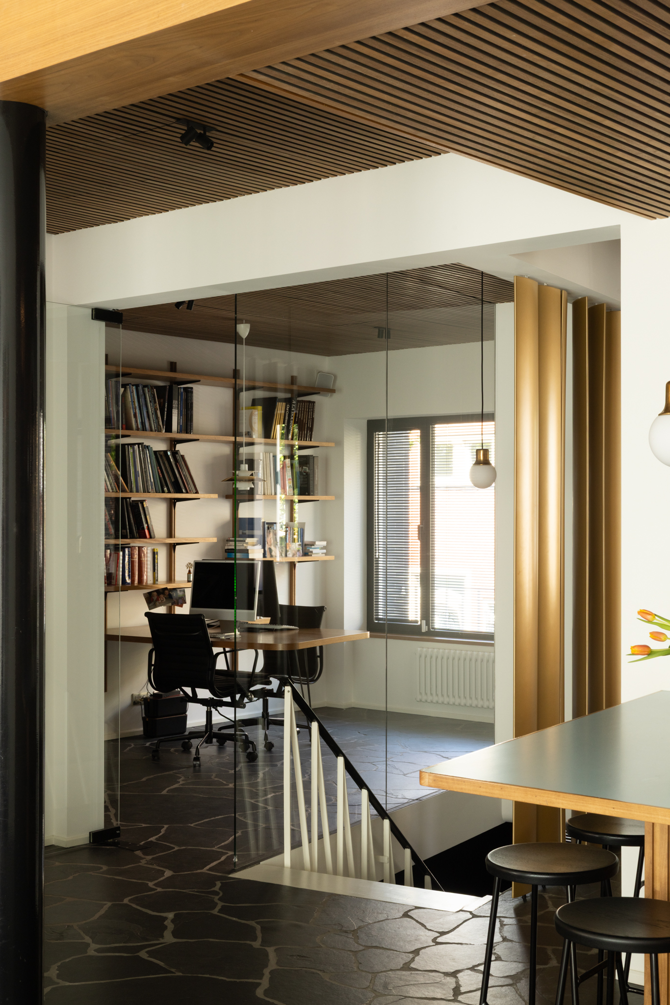 Claustra en laiton et parois vitrées dissimulant un espace bureau adjacent à la cuisine, une rénovation intérieure.