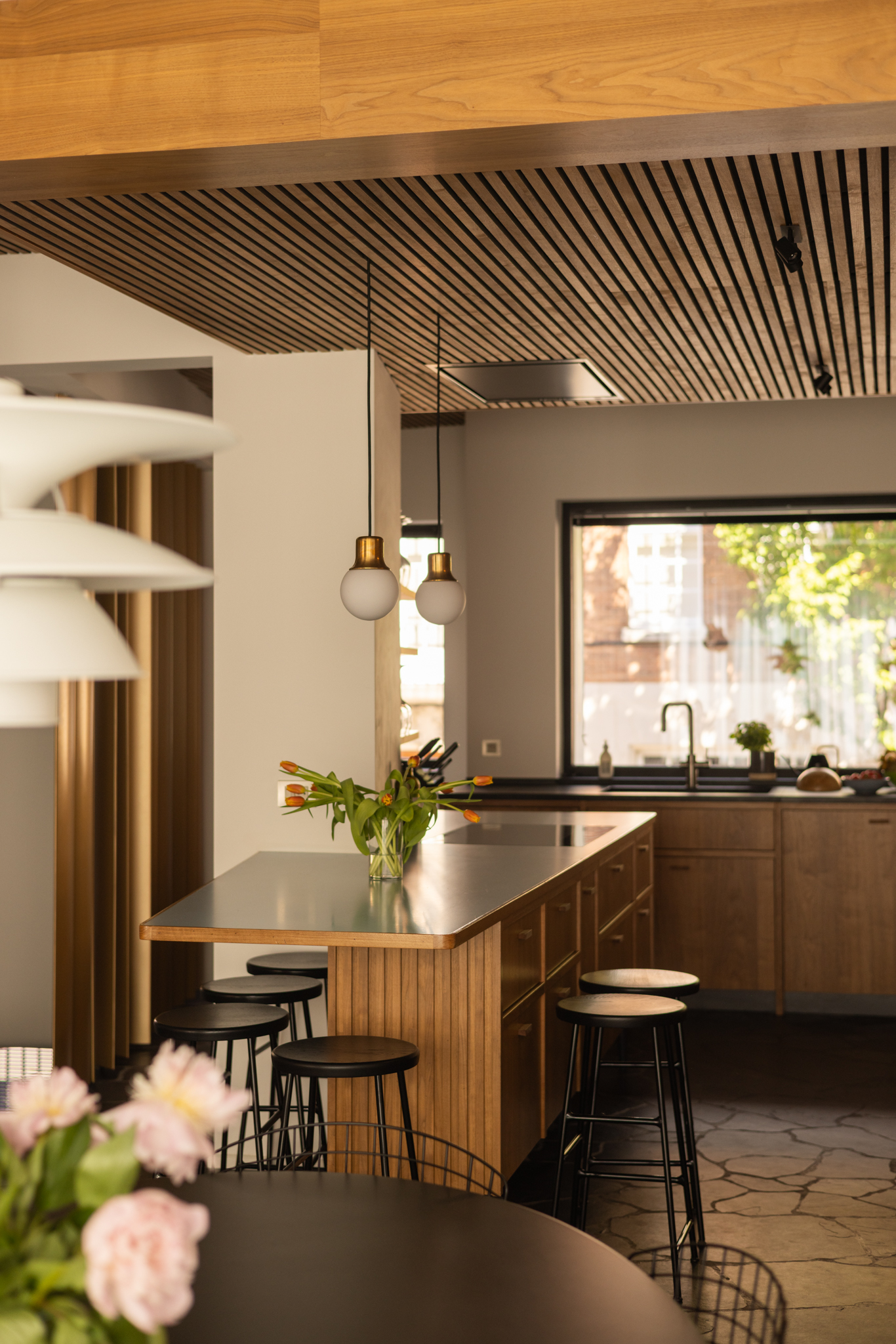 Cuisine en noyer sur mesure avec plans de travail en stratifié noir et bleu pâle, îlot central intégré autour d’une colonne existante, plafond acoustique